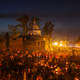 A church is seen in the background, illuminated by the glow of street lights and candles being held by people in a large crowd.